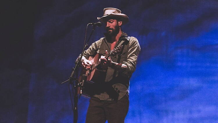 Close-up of a musician playing an acoustic guitar and singing into a microphone on a stage Close-up of a musician playing an acoustic guitar and singing into a microphone on a stage