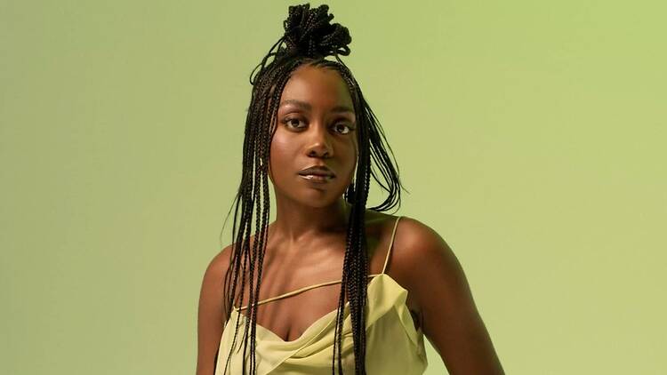 A close-up of a person posing in a yellow outfit against a green backdrop. A close-up of a person posing in a yellow outfit against a green backdrop.