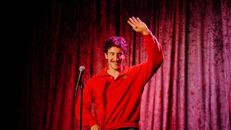 A wide shot of a person waving beside a microphone on a stage.