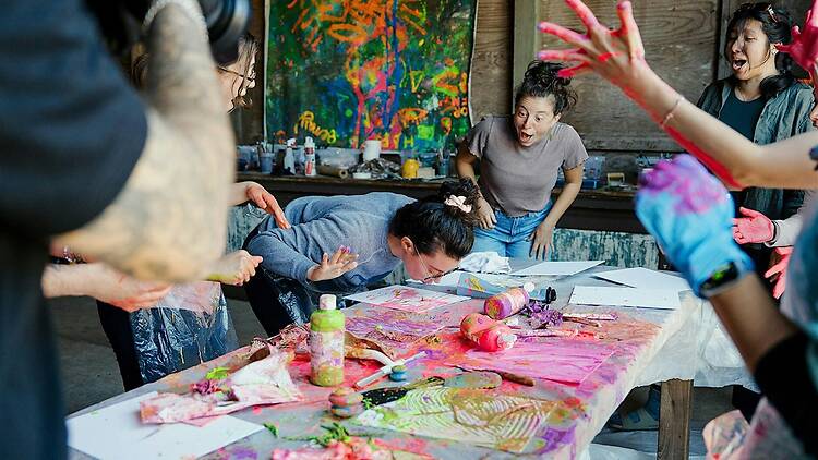 A wide shot of people painting together at a table during an indoor art activity.