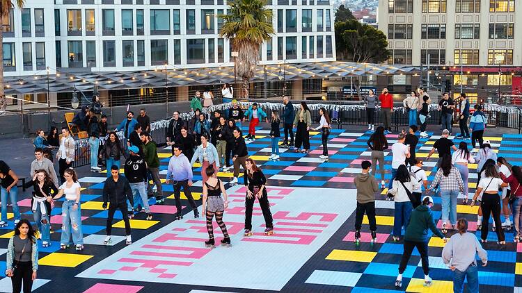 A wide shot of people roller skating together on a colorful rooftop plaza.