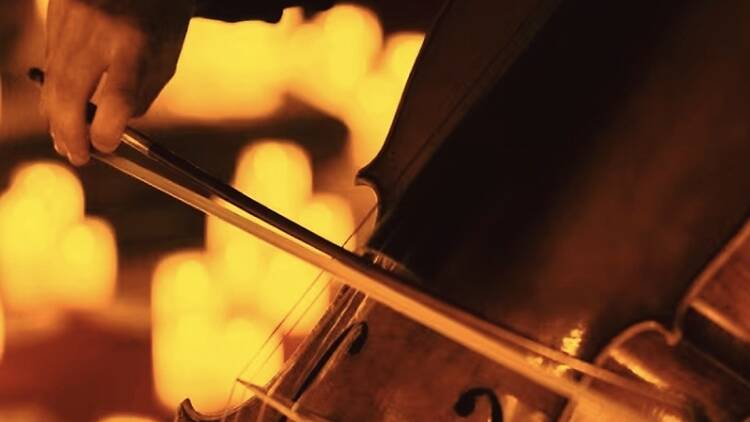 A close-up of a person playing a violin with a bow under warm lighting.