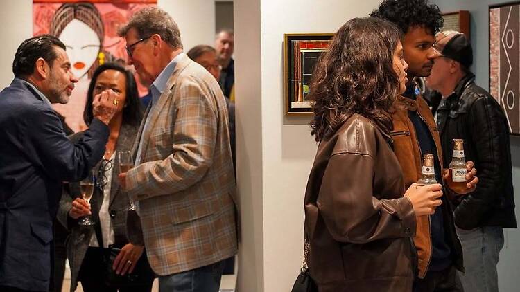 A wide shot of people viewing artwork and socializing at an art gallery exhibition A wide shot of people viewing artwork and socializing at an art gallery exhibition