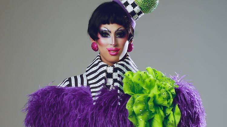 A close-up of a performer posing in a striped outfit with a feathered costume and glittering hat.