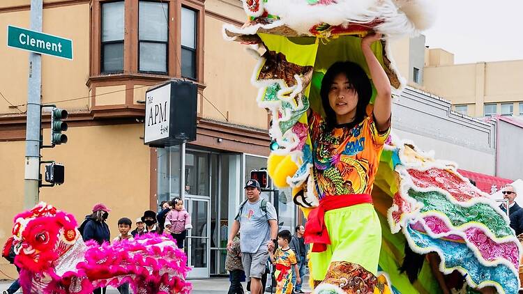 A wide shot of a performer carrying a lion dance costume during a street festival at a city intersection