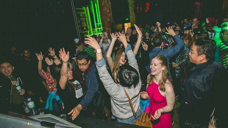 A wide shot of a crowd dancing and cheering at an indoor event under green lights. A wide shot of a crowd dancing and cheering at an indoor event under green lights.