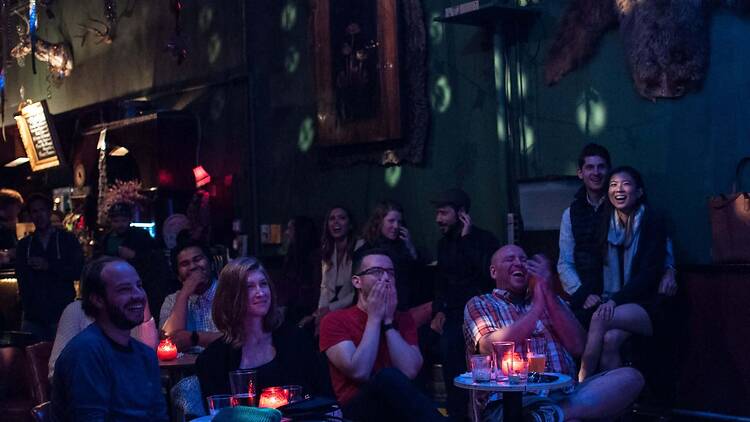 A wide shot of people laughing and applauding at an indoor comedy event. A wide shot of people laughing and applauding at an indoor comedy event.
