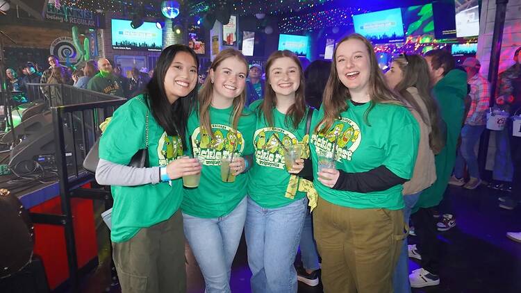 A medium shot of four people smiling and posing with drinks at an indoor event.
