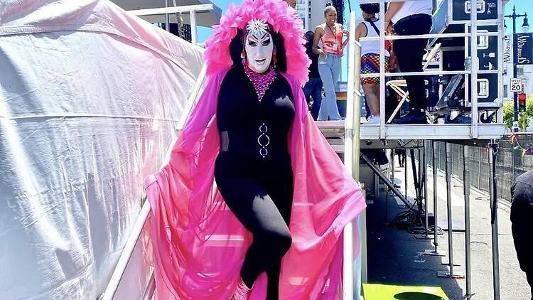 Performer in a black outfit and pink costume walks at an outdoor festival. Performer in a black outfit and pink costume walks at an outdoor festival.