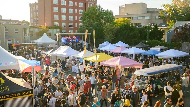 A wide shot of a large crowd browsing food and craft stalls at an outdoor festival. A wide shot of a large crowd browsing food and craft stalls at an outdoor festival.