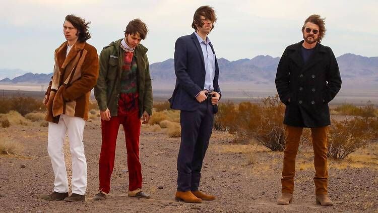 A wide shot of four people posing together in a desert landscape with mountains in the background. A wide shot of four people posing together in a desert landscape with mountains in the background.