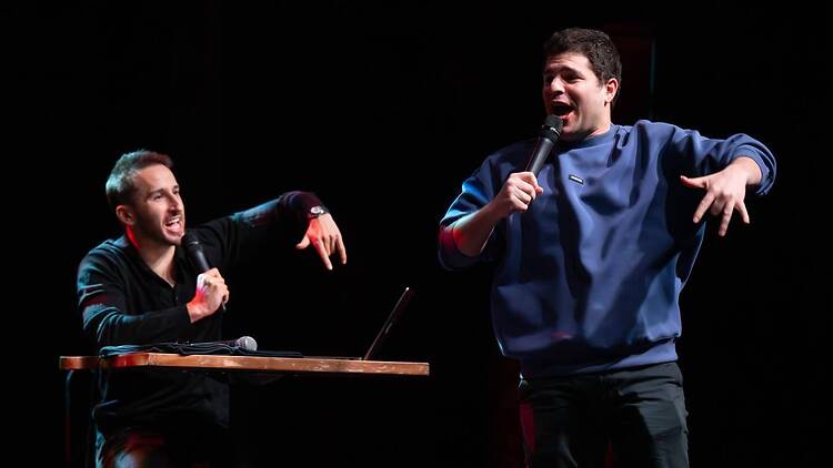 A wide shot of two comedians performing on stage with microphones.