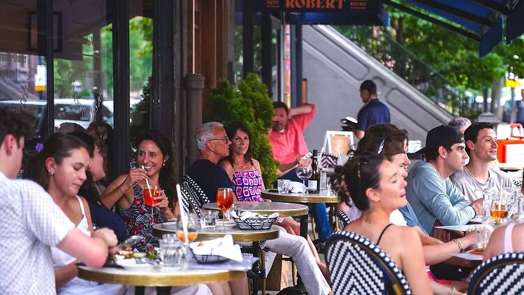 A wide shot of people dining and talking together at an outdoor restaurant. A wide shot of people dining and talking together at an outdoor restaurant.