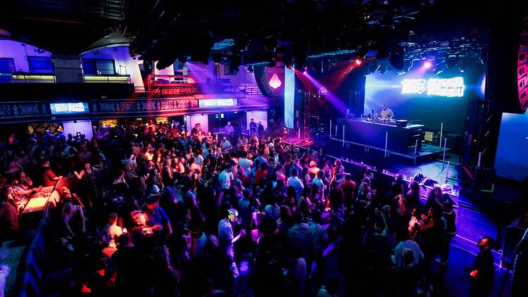 A wide shot of a DJ performing for a large crowd at an indoor nightclub. A wide shot of a DJ performing for a large crowd at an indoor nightclub.