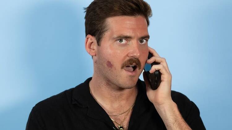 A close-up of a person speaking on a phone against a blue backdrop.