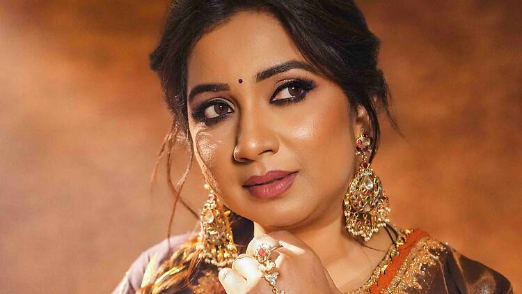 A close-up of a person posing in traditional Indian attire and jewelry against a warm backdrop. A close-up of a person posing in traditional Indian attire and jewelry against a warm backdrop.