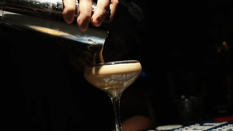 A close-up of a bartender pouring a foamy drink into a glass at a bar. A close-up of a bartender pouring a foamy drink into a glass at a bar.