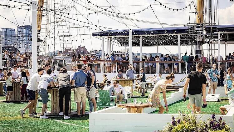 A wide shot of people socializing on a rooftop venue with a waterfront and city skyline. A wide shot of people socializing on a rooftop venue with a waterfront and city skyline.