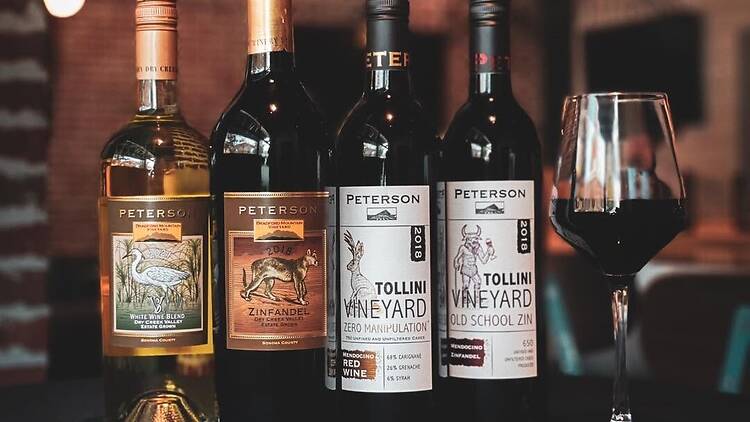 A close-up of wine bottles and a filled wine glass displayed on a bar counter.