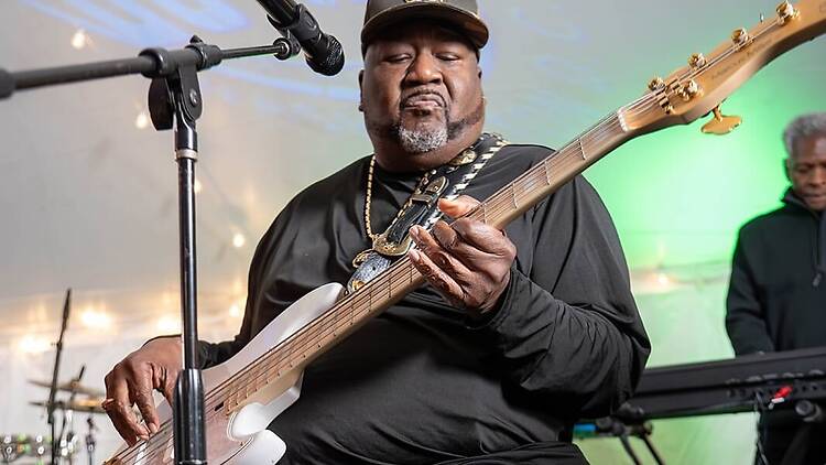 A close-up of a musician playing bass guitar on stage near a microphone. A close-up of a musician playing bass guitar on stage near a microphone.