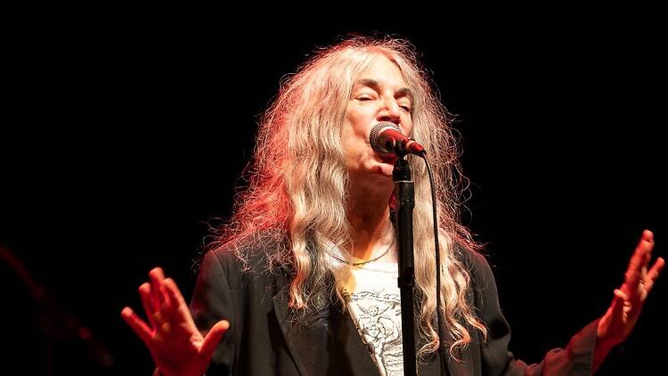 A close-up of a singer performing into a microphone with both hands raised on stage. A close-up of a singer performing into a microphone with both hands raised on stage.