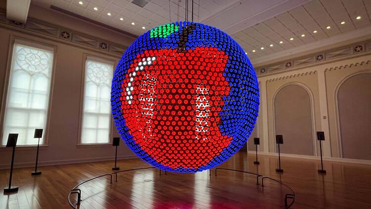 A wide shot of a large illuminated spherical art installation displayed in an indoor gallery.