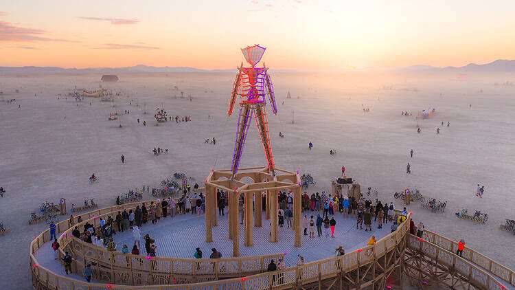 A wide shot of an illuminated art installation surrounded by people at sunset in a desert. A wide shot of an illuminated art installation surrounded by people at sunset in a desert.