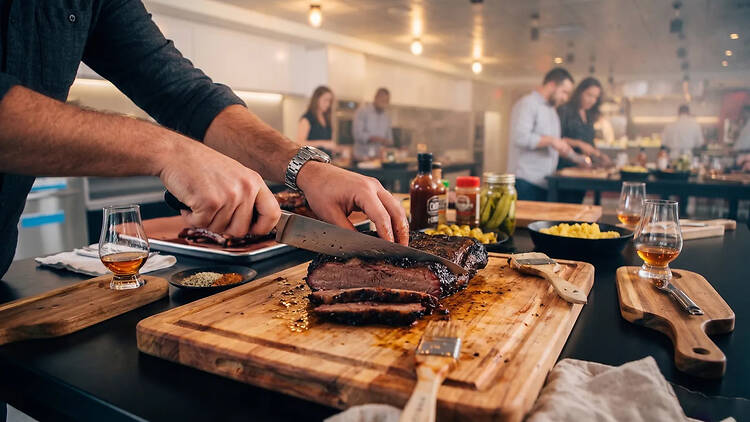 A close-up of a person slicing smoked brisket on a cutting board in a kitchen.