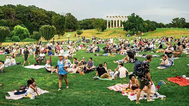 A wide shot of people relaxing on a grassy park lawn near a classical monument. A wide shot of people relaxing on a grassy park lawn near a classical monument.