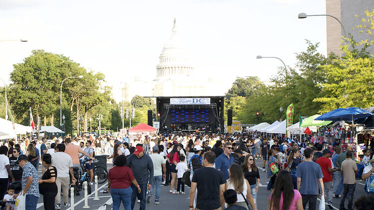 A wide shot of people browsing vendor booths and gathering at a street festival with a stage near the U.S. Capitol A wide shot of people browsing vendor booths and gathering at a street festival with a stage near the U.S. Capitol