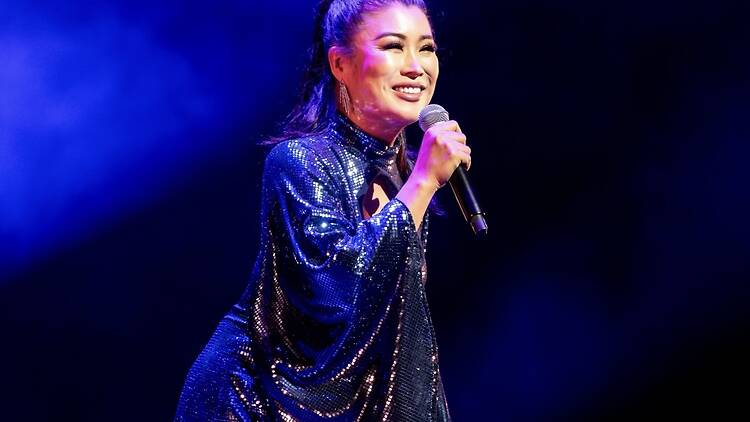 A wide shot of a singer performing into a microphone on stage under blue lighting. A wide shot of a singer performing into a microphone on stage under blue lighting.