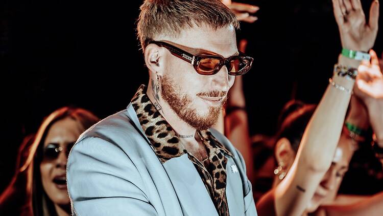 A medium shot of a person wearing sunglasses and a light blue outfit among a cheering crowd. A medium shot of a person wearing sunglasses and a light blue outfit among a cheering crowd.