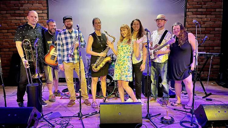 A wide shot of eight musicians posing together on stage with instruments. A wide shot of eight musicians posing together on stage with instruments.
