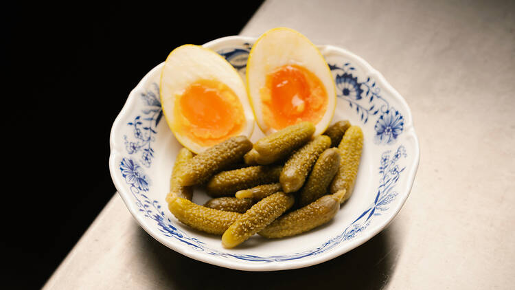 Hard-Boiled Eggs and Pickles at Bar Kabinett, Stockholm Soft-boiled eggs halved next to small green gherkin pickles served in a patterned porcelain bowl at Bar Kabinett.