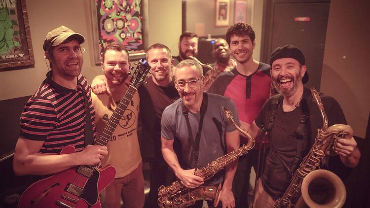 Group of smiling musicians posing with guitars and saxophones backstage. Group of smiling musicians posing with guitars and saxophones backstage.
