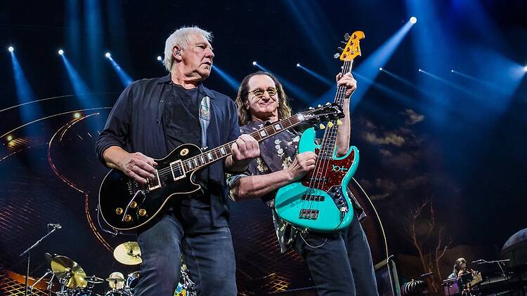 Wide shot of two musicians playing guitars on stage under blue concert lights. Wide shot of two musicians playing guitars on stage under blue concert lights.