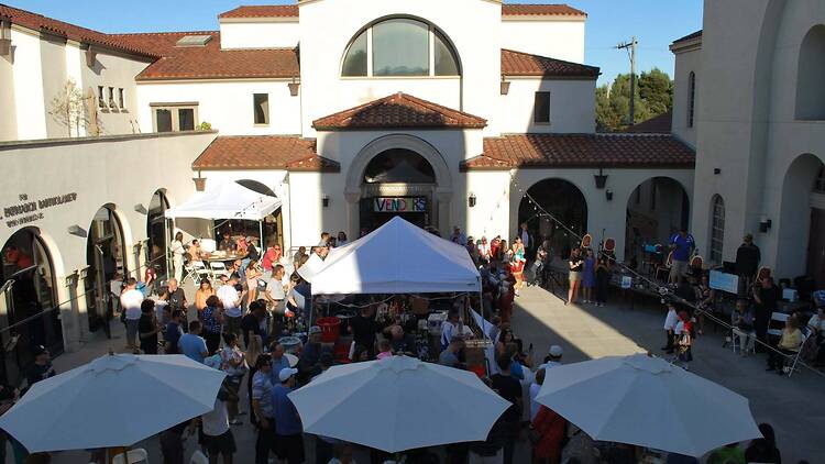 Wide view of guests gathering under tents and umbrellas at an outdoor courtyard event.