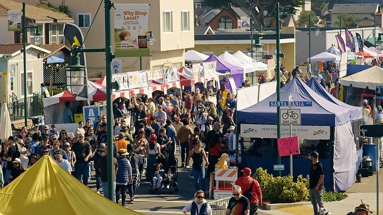 Wide view of a crowded outdoor street festival with attendees walking among vendor tents. Wide view of a crowded outdoor street festival with attendees walking among vendor tents.