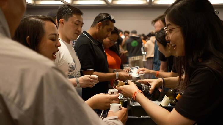 Close-up of attendees sampling drinks at an indoor tasting event. Close-up of attendees sampling drinks at an indoor tasting event.