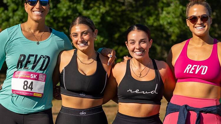 A wide shot of four participants posing together outdoors at a 5K fitness event A wide shot of four participants posing together outdoors at a 5K fitness event