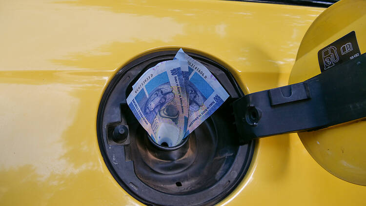 Symbol for high fuel price - 100 Rand  bills sticking out of a car's fuel tank, economic financial concept
