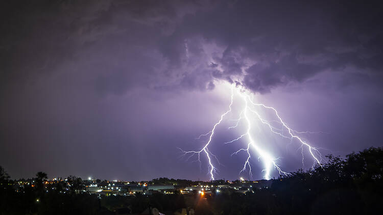 A stunning photograph of a lightning strike over a suburban area during a vibrant sunset 2189068414