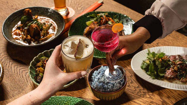 People clinking glasses over a table of food.