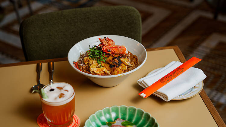 A bowl of noodles and a cocktail on a table.