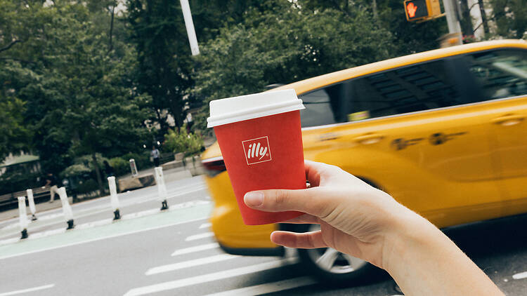 illycaffé in someone's hand in front of a cab on a crosswalk illycaffé in someone's hand in front of a cab on a crosswalk