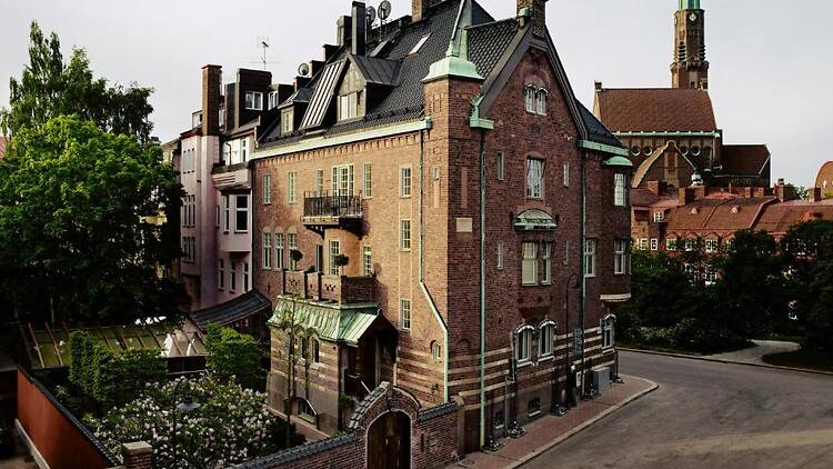 Exterior view of the historic red brick building of Ett Hem luxury hotel in Stockholm featuring a private courtyard and church tower background.