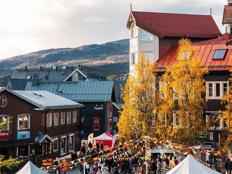 Autumn Market in Åre, Sweden Vibrant autumn market setup in the village square of Åre, Sweden, featuring colorful bunting, market stalls, golden trees, and mountain views.