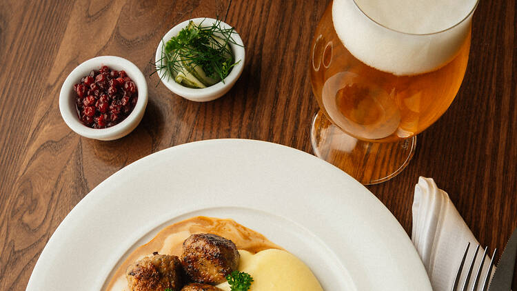 Stockholm, Söderhallarna, Kafé Söder Meatballs with mashed potatoes and cream sauce, lingonberries, pickled cucumber and a glass of beer on a wooden table.