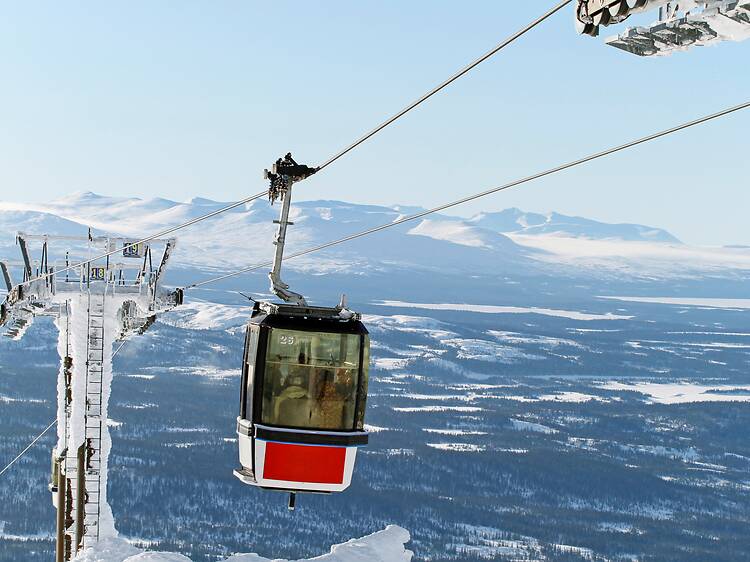 Cable car ascending Mount Åreskutan with panoramic views of Åre A red and white cable car rides past icy lift pylons with snow-covered mountains and a frozen valley in the background in Åre, Sweden