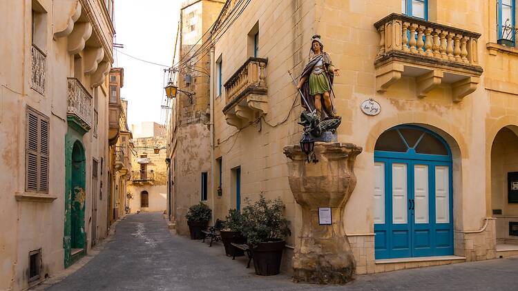 Statue of Saint George in Victoria, with traditional Maltese architecture in the background Statue of Saint George in Victoria, with traditional Maltese architecture in the background